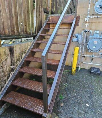 Close up of an exterior staircase that displays failing paint and rust starting to develop.