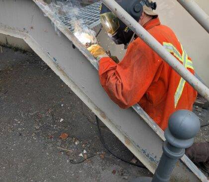 A welder welding new treads on to the existing staircase structure,